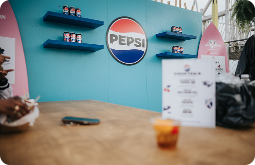 Pepsi-branded display with blue shelves holding cans and a large logo on a teal wall at an event booth.