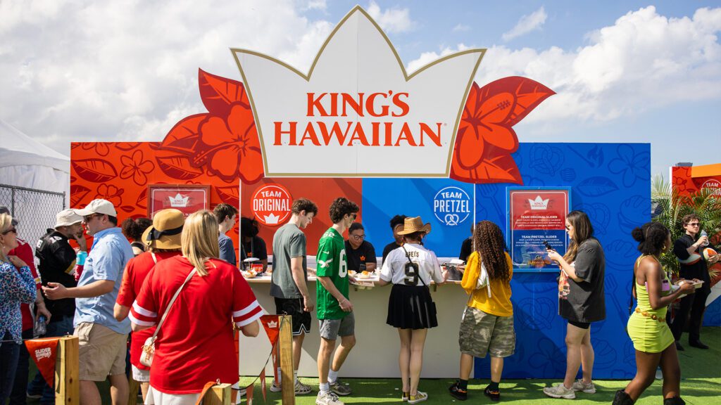 Crowd gathers at a colorful King’s Hawaiian booth featuring “Team Original” and “Team Pretzel” sections at an outdoor event.