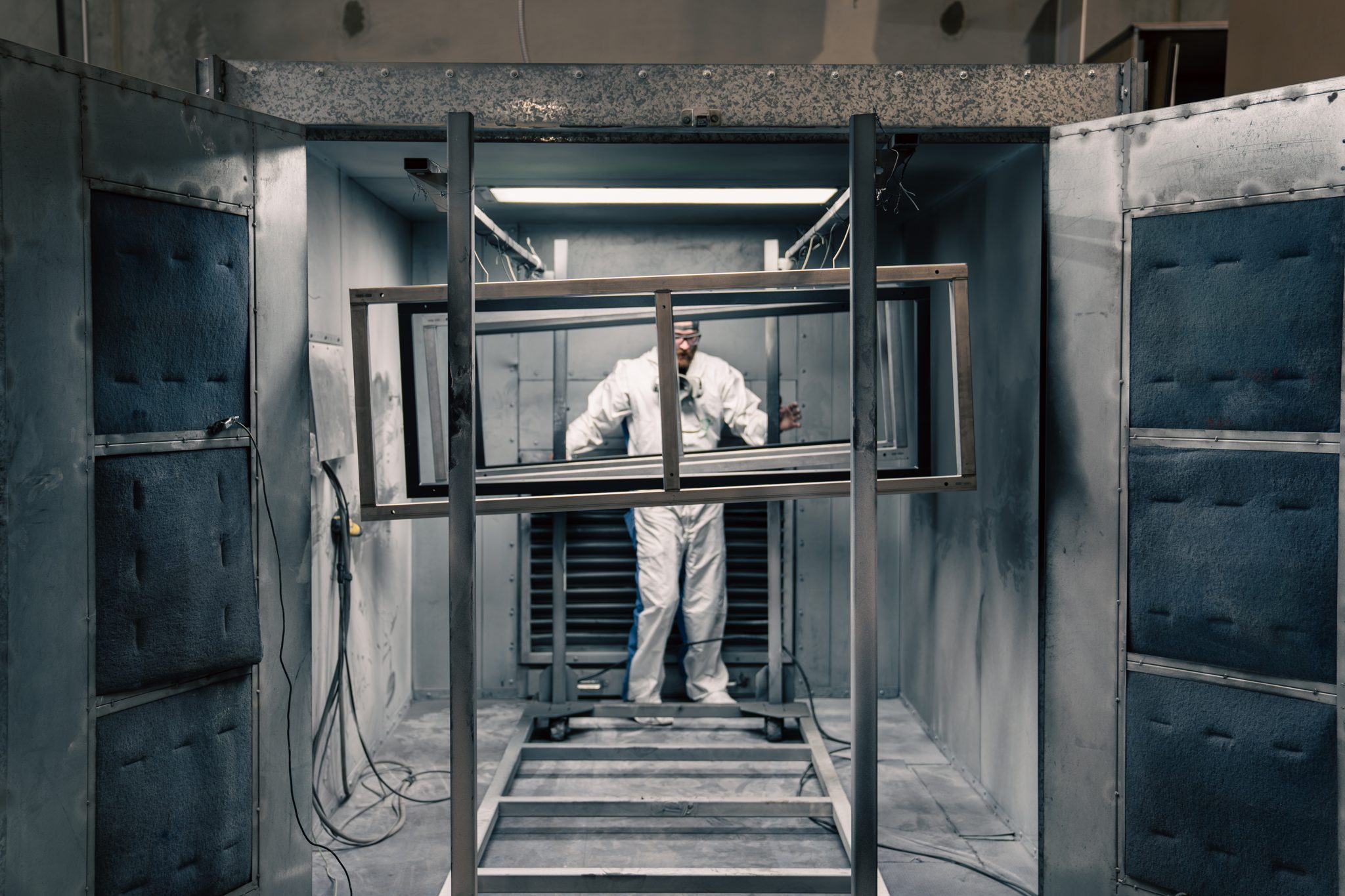 Technician spraying powder coat on a steel display frame in the Steadfast booth