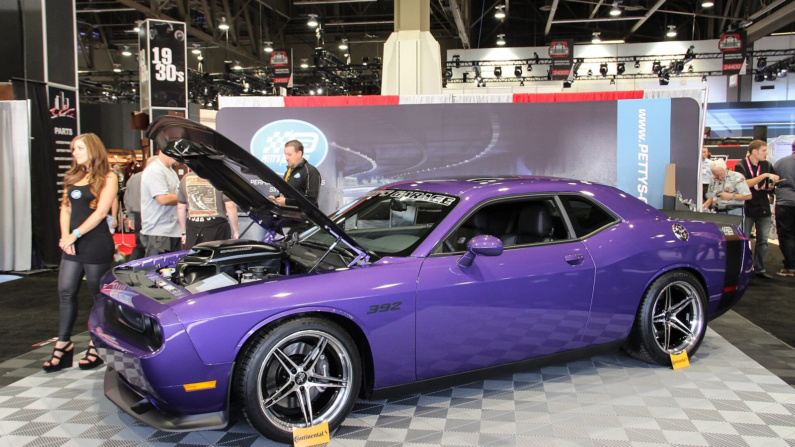 Display vehicle inside a SEMA Show exhibitor booth with staff and attendees